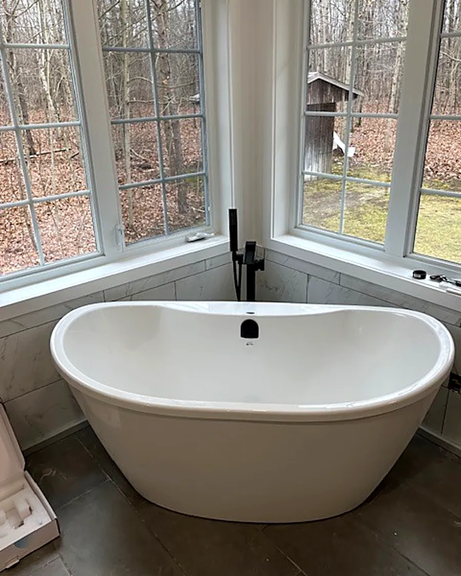 Freestanding soaker tub with a floor-mounted black faucet beside a bay window